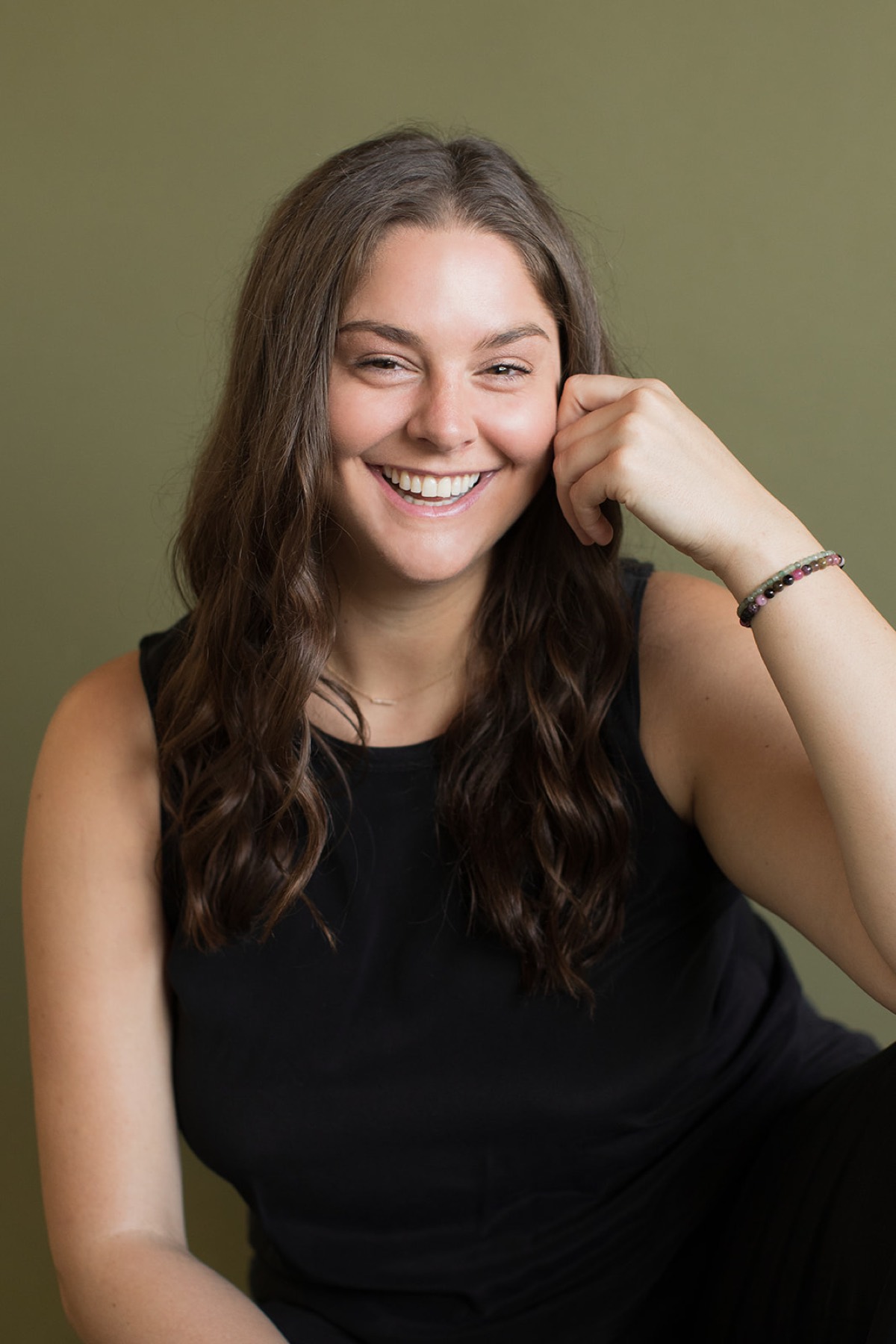Heather Flynn laughing warmly, resting her head on her hand against an olive-green studio backdrop